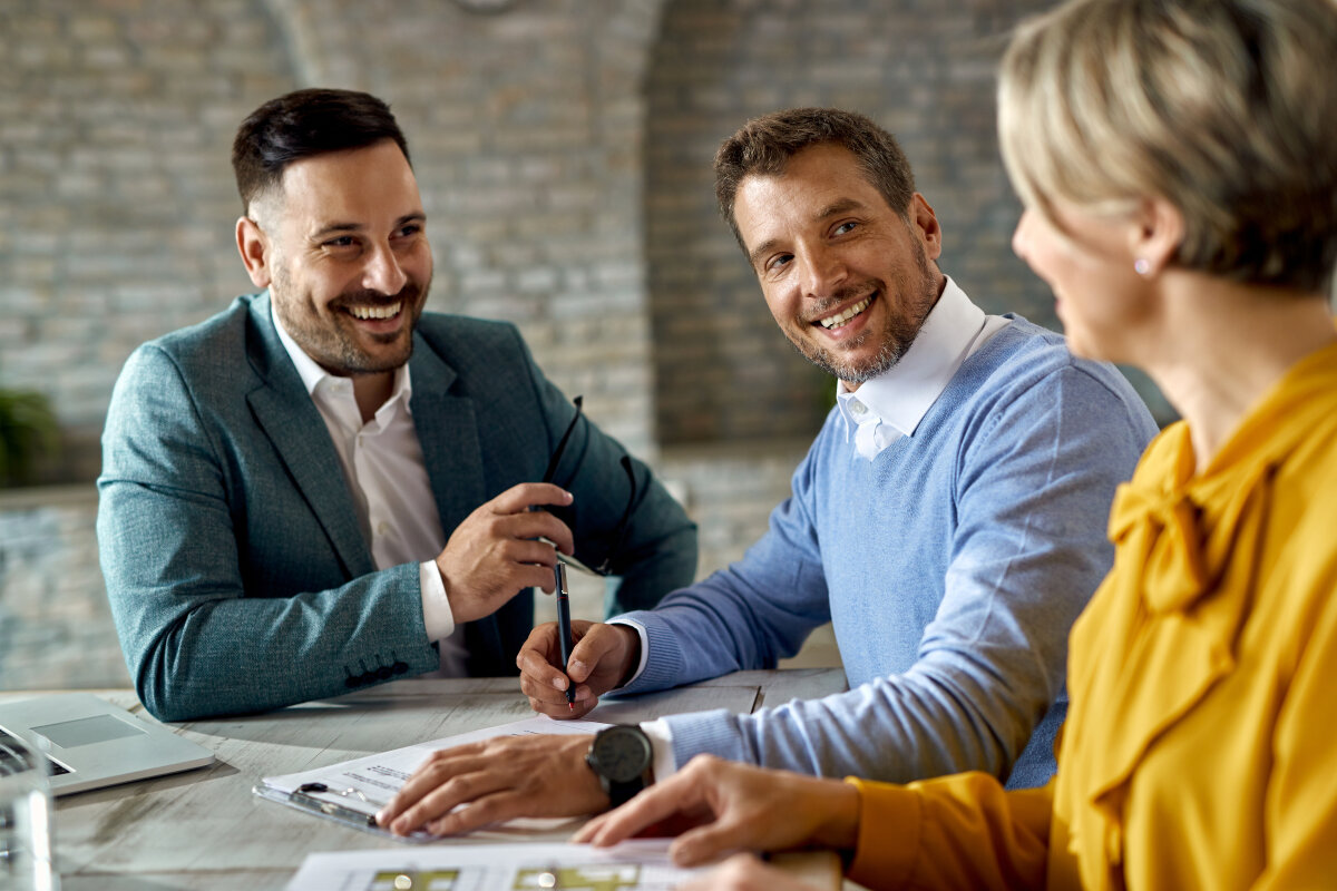 Happy man signing a contract while being with his wife on a meeting with financial advisor.